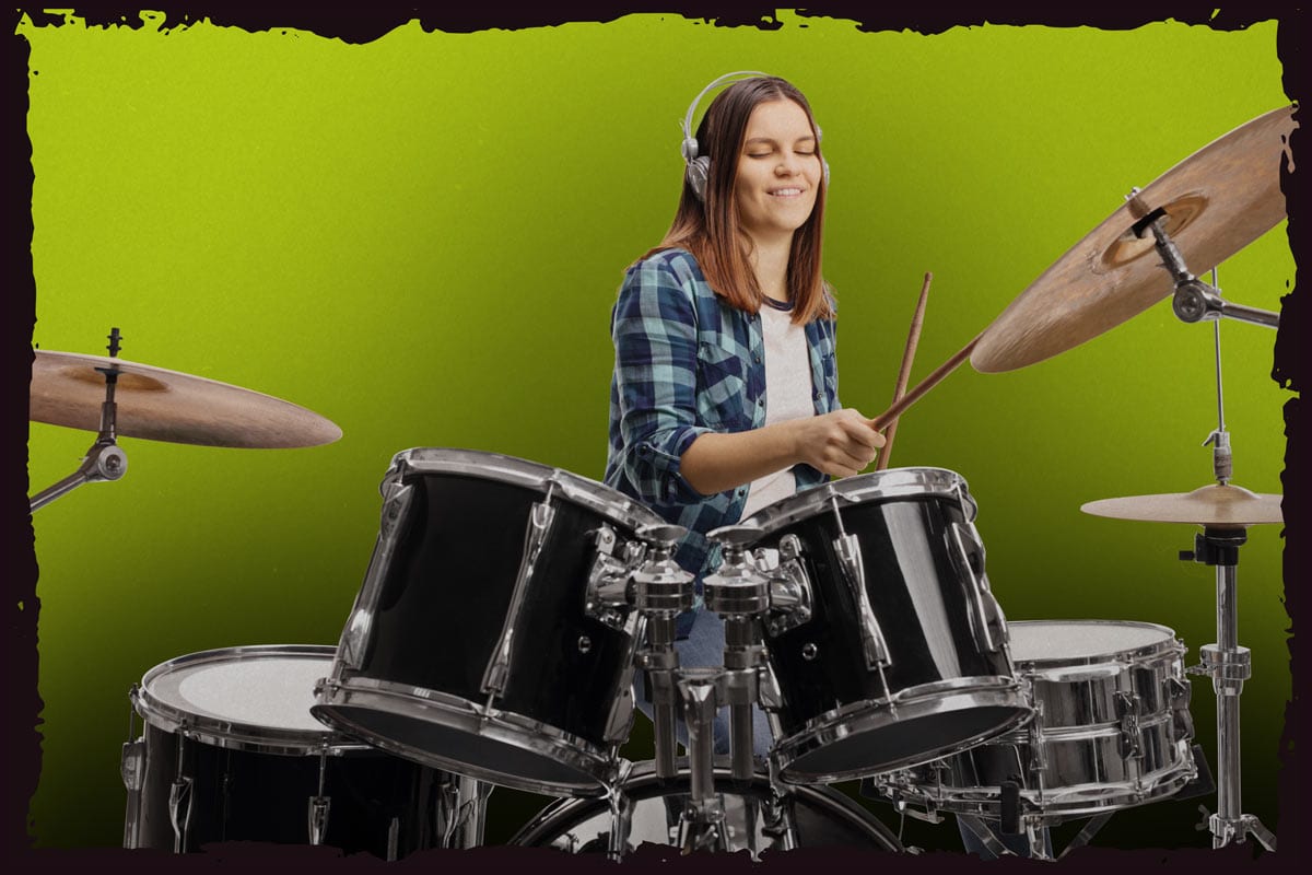 Female teen wearing a blue plaid shirt and headphones playing an acoustic drum set.