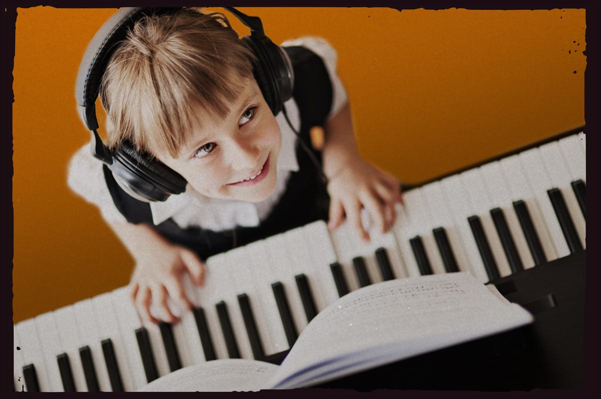 An overhead shot of a young girl wearing a school uniform and headphones looking up and smiling from an electric keyboard.