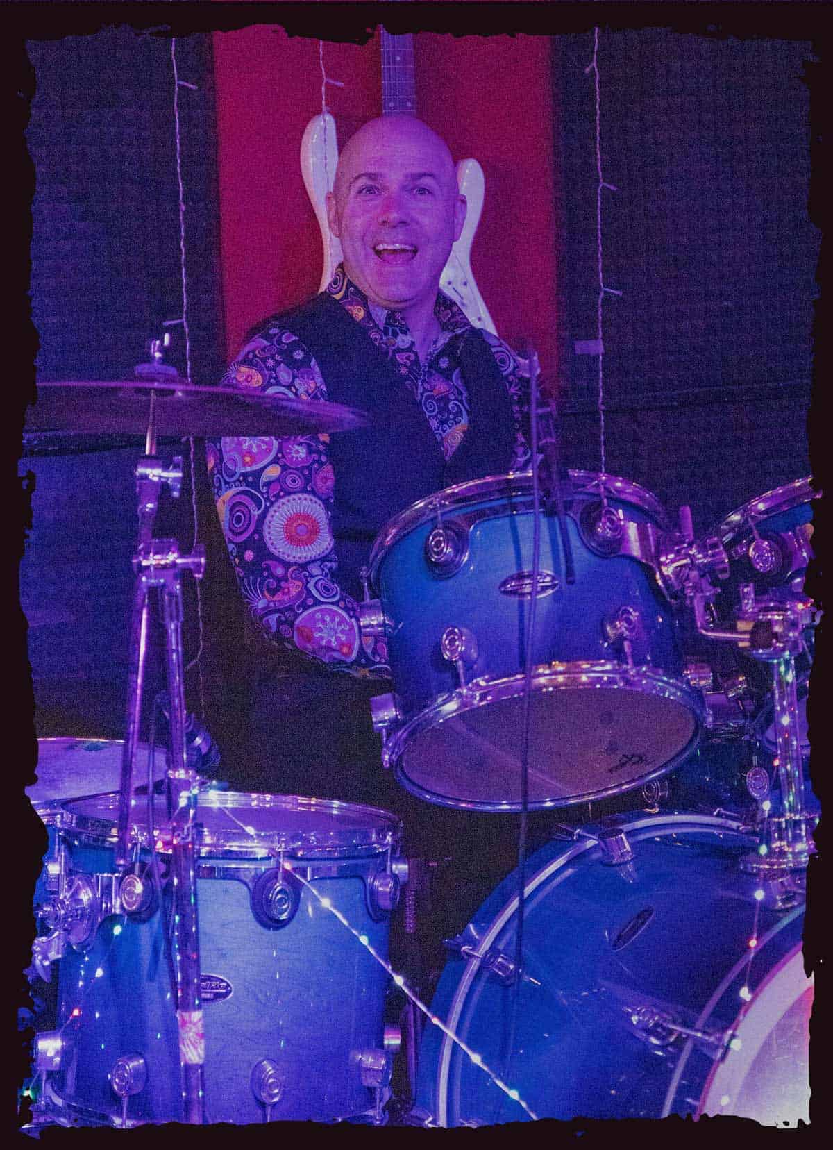 A closeup of Barrett smiling while playing acoustic drums on stage.